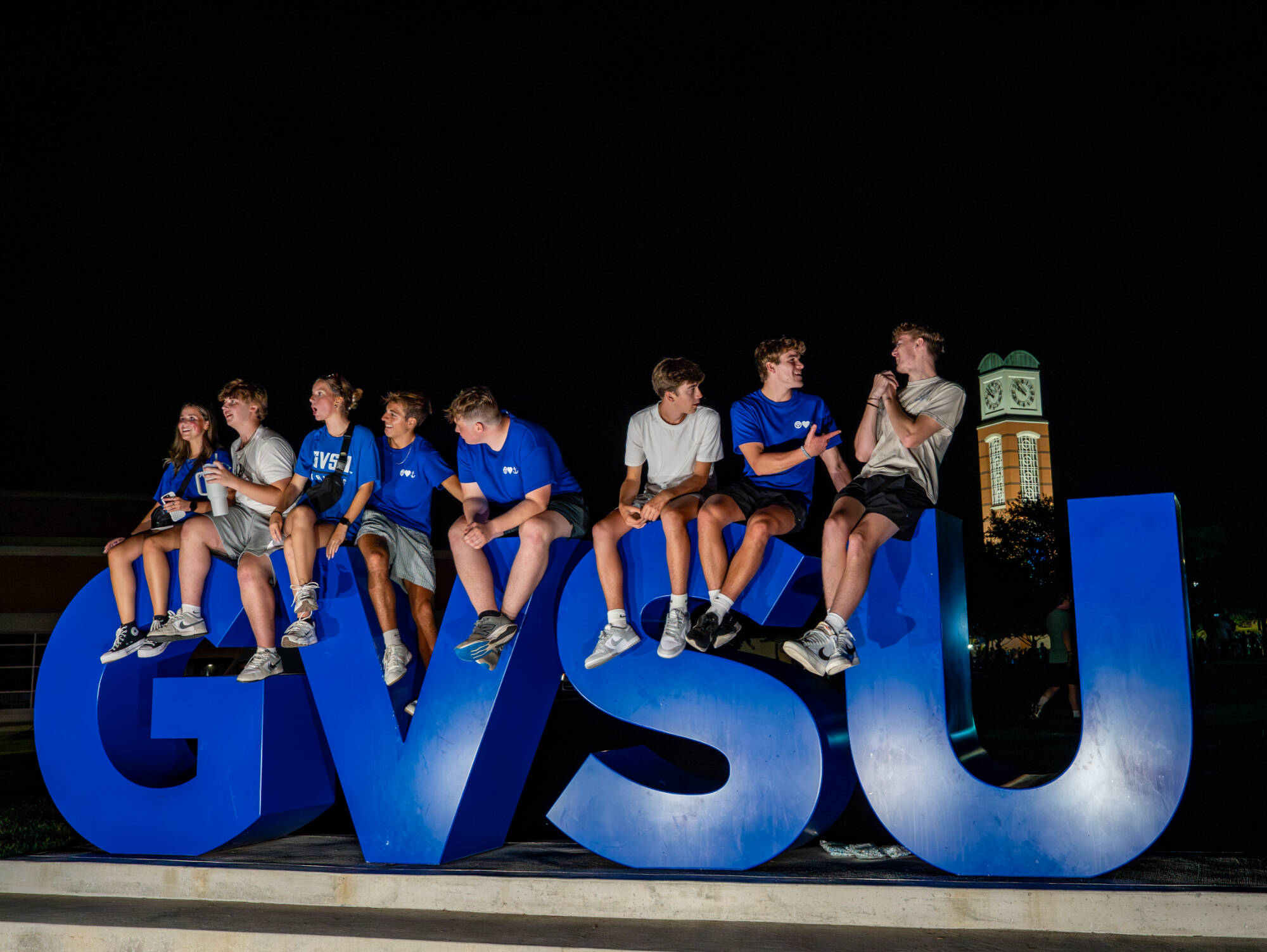 Eight Students Sitting on the "GVSU" Sign Post